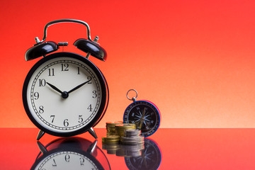 Alarm Clock, compass and coins on red background with selective focus and crop fragment. Copy space  and business concept