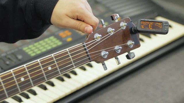 Process of tuning acoustic guitar with electronic tuner close up