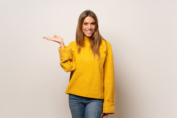 Woman with yellow sweater over isolated wall holding copyspace imaginary on the palm to insert an ad