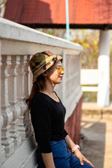 Women white skin lovely brown hair red lips black shirt wearing a blue gene woman helmeted wearing yellow glasses stand  poses photography portrait which has water in back in the park.