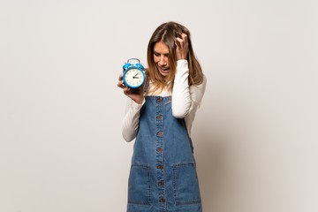 Beautiful woman over isolated white wall restless because it has become late and holding vintage alarm clock