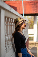 Women white skin lovely brown hair red lips black shirt wearing a blue gene woman helmeted wearing yellow glasses stand  poses photography portrait which has water in back in the park.