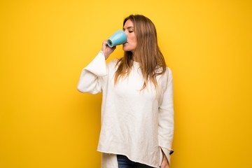 Blonde woman over yellow wall holding a hot cup of coffee