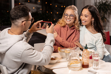 Two female friends asking man to take a picture of them in eating house.