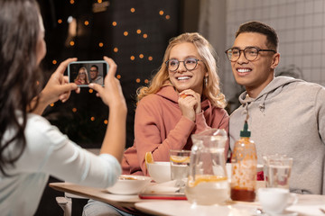Girl taking picture of familiar couple on her phone while they sitting and smiling.