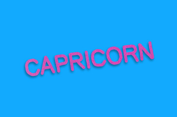 Word capricorn cut out of purple paper on blue table. Top view. Horoscope concept