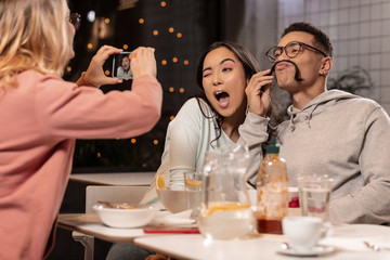 Three young adults sitting in cafeteria and fooling around for photo.