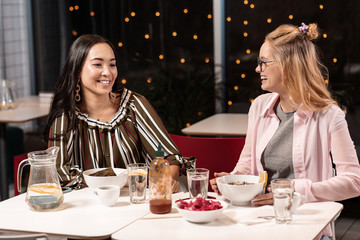 Two female friends sitting and chatting with enthusiasm in cafe over lunch.