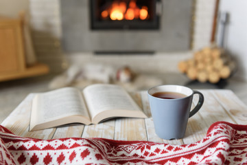 Book and cup of tea near burning fireplace. Hygge concept