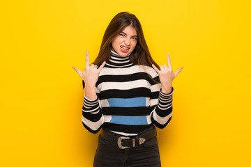 Young woman over yellow wall making rock gesture