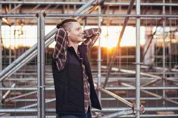 Fototapeta premium Cute young male hipster posing against a background of barred building with iron structures. The concept of tourist walks around the city
