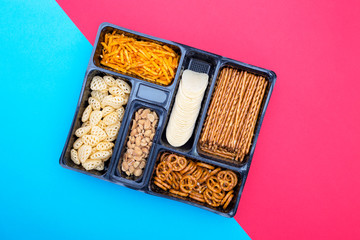 Box with a set of snack on a colored background, top view