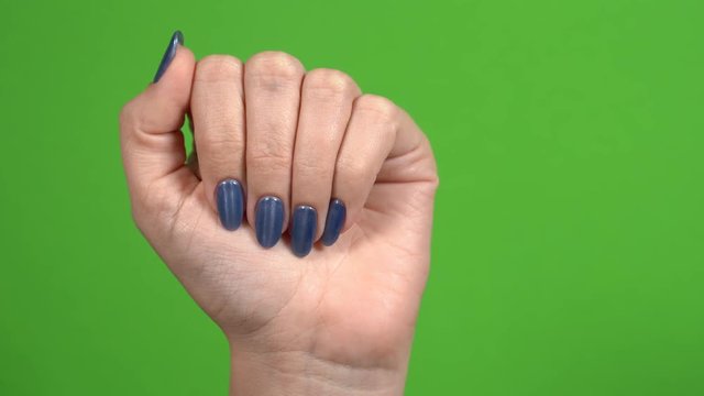 Closeup view of beautiful female hands with blue glossy professional manicure with cat eye effect isolated on green background. 4k video footage.
