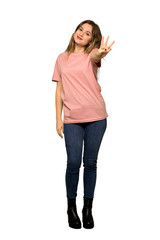 A full-length shot of a Teenager girl with pink sweater happy and counting three with fingers on isolated white background