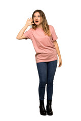 A full-length shot of a Teenager girl with pink sweater listening to something by putting hand on the ear on isolated white background