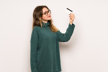 Teenager girl over white wall holding a credit card and thinking