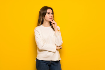 Teenager girl over yellow wall thinking an idea while looking up