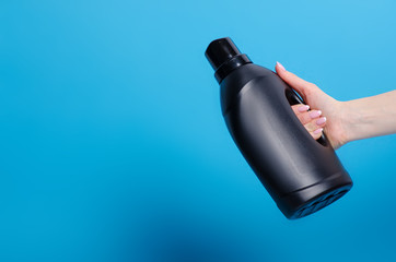 Black bottle laundry gel in hand on blue background isolation