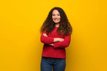 Teenager girl with red sweater over yellow wall keeping the arms crossed in frontal position
