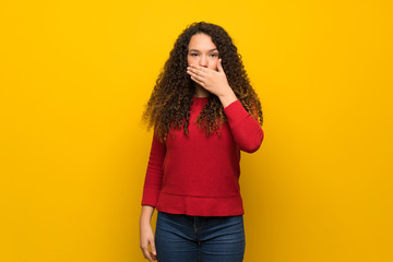 Teenager girl with red sweater over yellow wall covering mouth with hands for saying something inappropriate