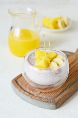 Chia pudding with mango pulp  in beautiful glasses with green mint leaves and cut fresh ripe tropical fruit, orange juice for breakfast on a light background - raw vegetarian sweet organic dessert. 