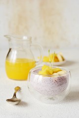 Chia pudding with mango pulp  in beautiful glasses with green mint leaves and cut fresh ripe tropical fruit, orange juice for breakfast on a light background - raw vegetarian sweet organic dessert. 