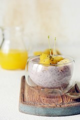 Chia pudding with mango pulp  in beautiful glasses with green mint leaves and cut fresh ripe tropical fruit, orange juice for breakfast on a light background - raw vegetarian sweet organic dessert. 