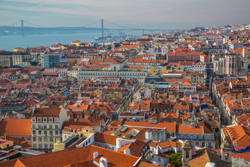 Fototapeta na wymiar View of the streets and the orange roofs of the old town. Lisbon, Portugal. In the distance, see the bridge of April 25 and the statue of Christ. View from the walls of the castle of St. George