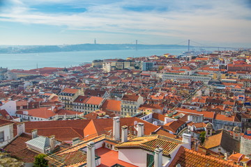 Fototapeta na wymiar View of the streets and the orange roofs of the old town. Lisbon, Portugal. In the distance, see the bridge of April 25 and the statue of Christ. View from the walls of the castle of St. George