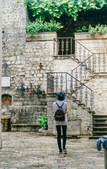 Fototapeta na wymiar The girl walks through the old European city against the backdrop of greenery and an iron staircase.
