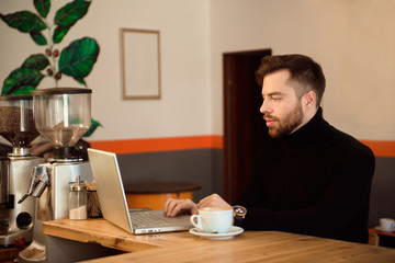 Businessman using laptop with tablet on wooden table in coffee shop with a cup of coffee.