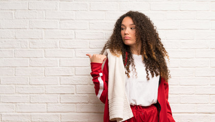 Teenager sport girl with curly hair unhappy and pointing to the side