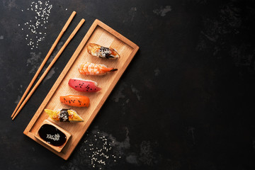 Assorted sushi set on a wooden plate, dark stone background. Japanese food sushi, soy sauce, chopsticks. Top view, copy space.