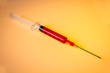 Fototapeta premium Syringe with blood on orange background
