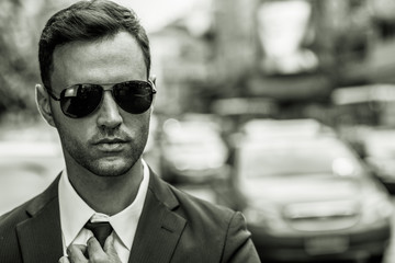 Portrait of a young man wearing sunglasses, shirt, suit and holding his tie