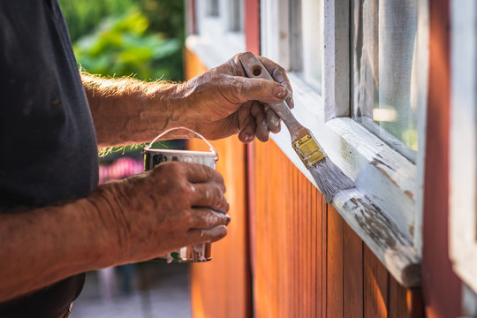House improvement. Senior craftsperson is painting wooden window frame using paintbrush.