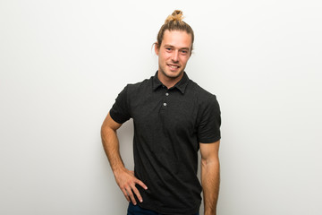 Fototapeta premium Blond man with long hair over white wall posing with arms at hip and smiling