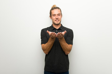 Blond man with long hair over white wall holding copyspace imaginary on the palm to insert an ad