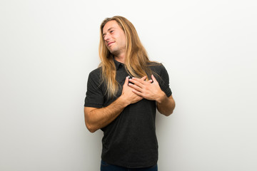 Blond man with long hair over white wall having a pain in the heart