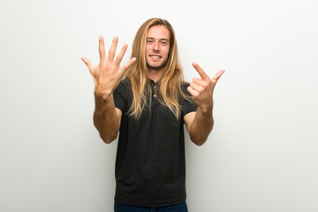 Blond man with long hair over white wall counting seven with fingers