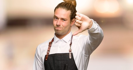 Barber man in an apron showing thumb down sign with negative expression in a barber shop