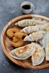 Wooden serving tray with different types of fried potstickers and panko breaded shrimps, closeup, vertical shot