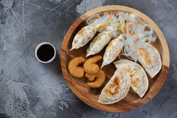 Fried korean potstickers with king shrimps in panko breading and noodles salad. Flatlay on a grey concrete background with space