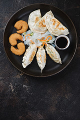 Fried potstickers with king shrimps in panko breading and noodles salad. Top view on a dark brown stone background with space