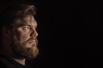 Close-up face profile portrait strong serious brutal bearded man on black. Confident and dramatic concept
