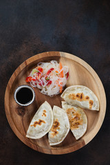 Wooden serving tray with fried potstickers, funchoza noodles salad and soy sauce. Flatlay on a dark brown metal surface with copyspace