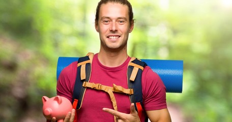 Hiker man with mountain backpacker holding a piggybank in the mountain