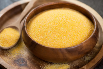Wooden bowl with raw polenta on a wooden serving tray, close-up, studio shot
