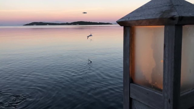 street lamp and sea, romantic pink light with sunset backgraound, pink orange weather, blue sky and birds flying