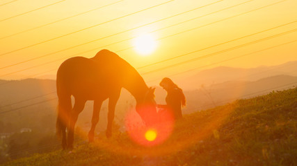 SUN FLARE: Happy young woman bonding with her stallion in a pasture at sunrise.